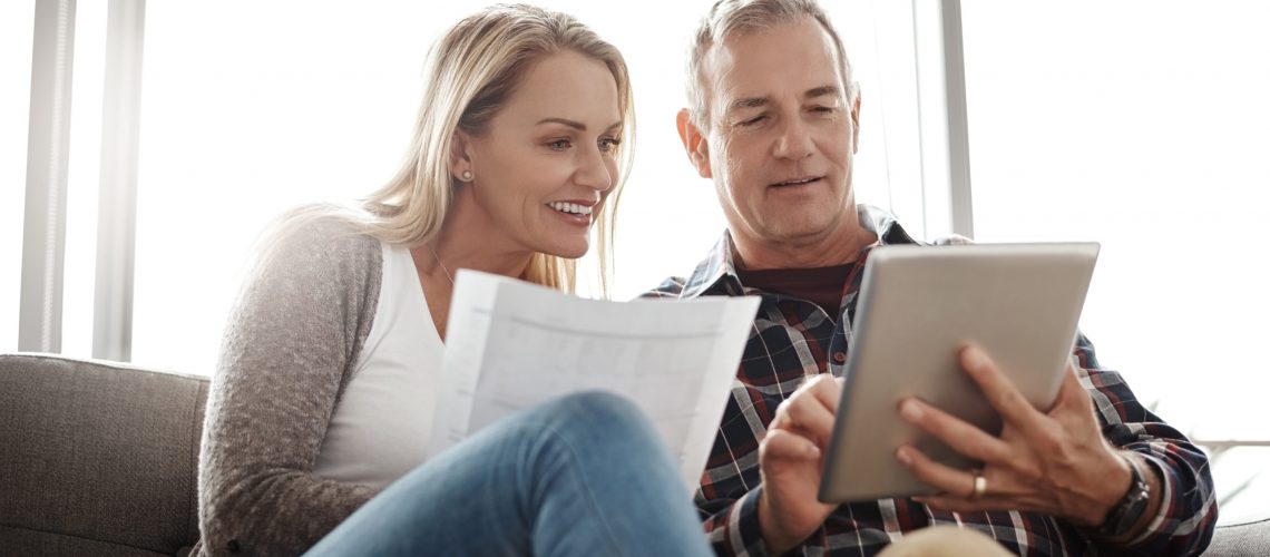 Shot of a mature couple using a digital tablet while going through their paperwork together on the sofa at home