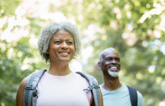 Senior woman smiles while hiking in woods with her husband